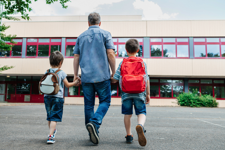 Back to school. View from the back of a happy dad escorts his sons schoolchildren to school. Parental care for children