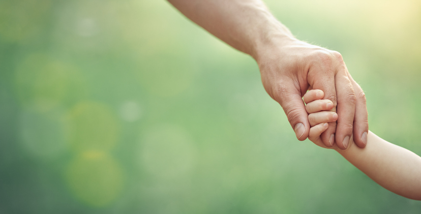 Fathers hand holding his little child in sunny day outdoor, united family and happy childhood concept, banner format.